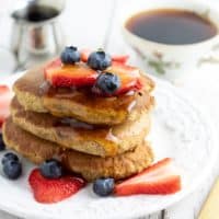 Banana oatmeal pancakes topped with blueberries and strawberries on white plate