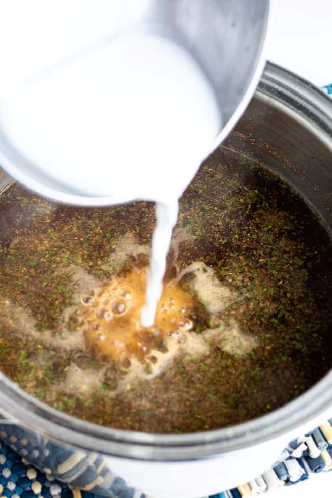 flour thickener being poured into brown gravy in pan