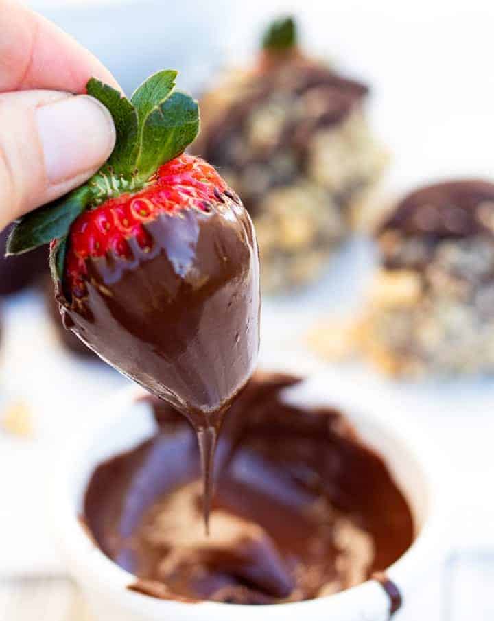 Hand dipping strawberry in chocolate in white bowl