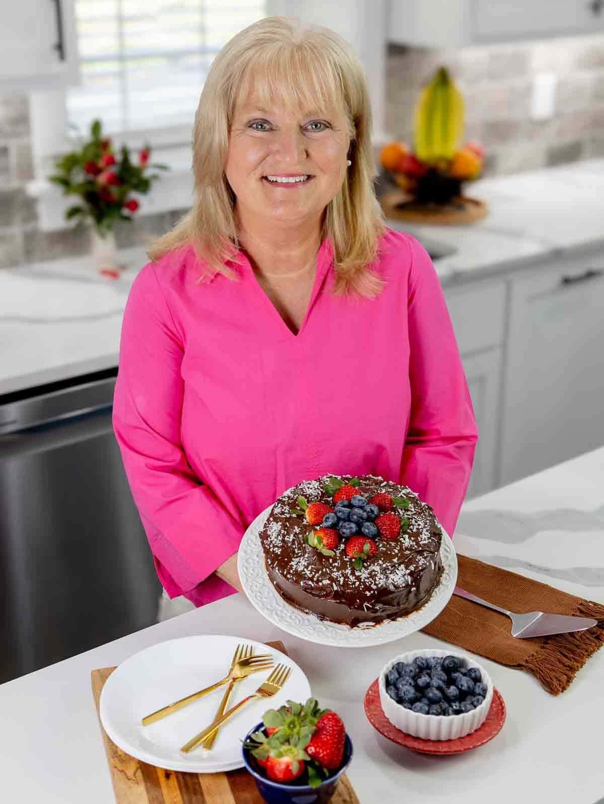 terri edwards displaying a vegan sweet potato chocolate cake in her kitchen.