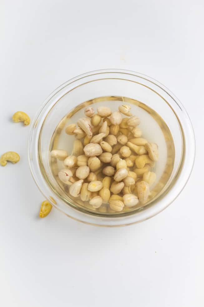 raw cashews soaking in a bowl of water on white background