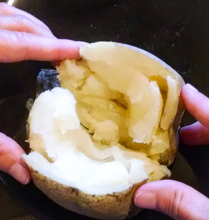 persons hand wrapped around sliced baked potato
