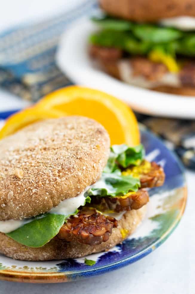 smoked tempeh bacon on english muffin with lettuce with orange slices on plate