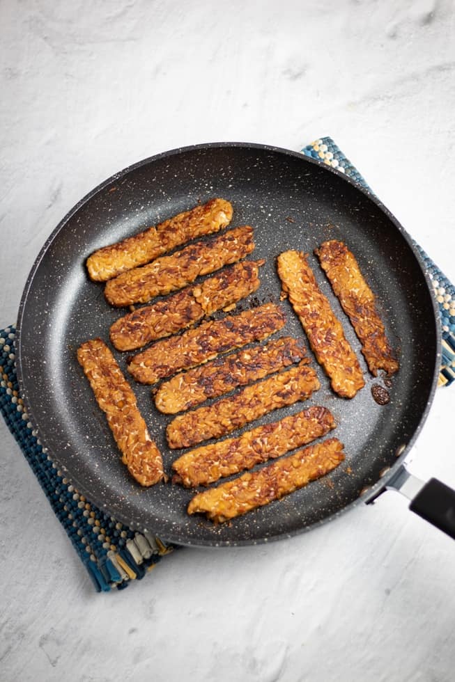 tempeh bacon in non stick pan on white background