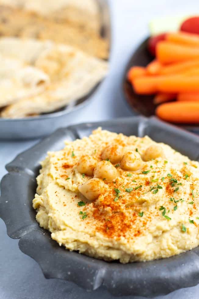 vegan hummus in metal bowl with pita bread in background