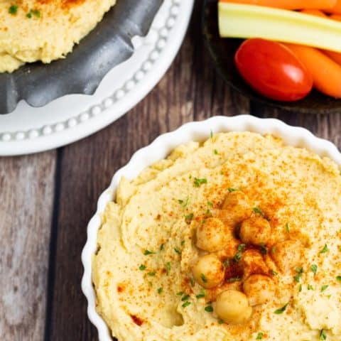 hummus in scalloped white bowl on wooden table background