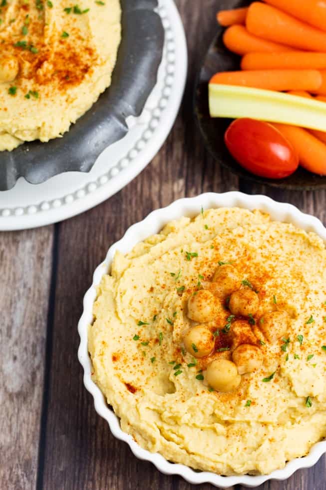 hummus in scalloped white bowl on wooden table background