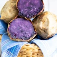 purple potato sliced in half in a basket with other potatoes