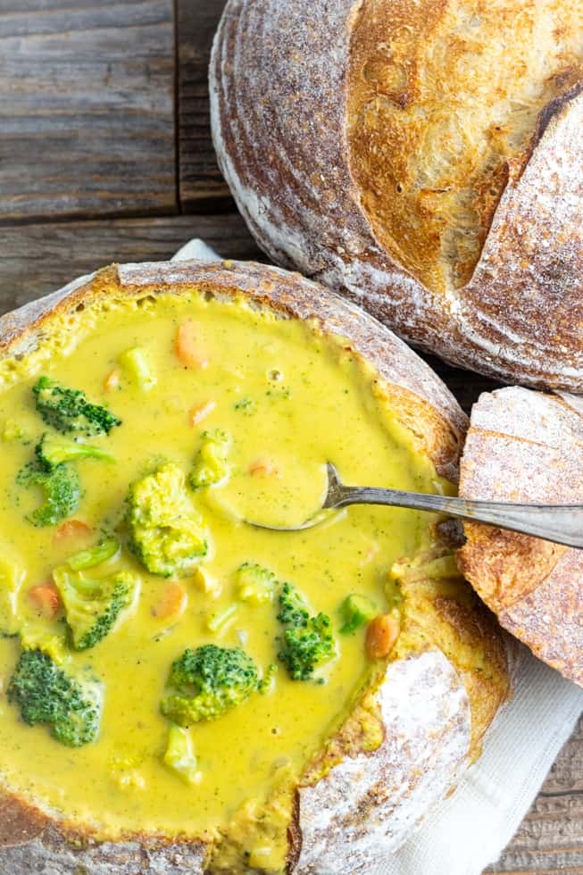 overhead shot of vegan broccoli cheese soup in bread bowl being spooned out
