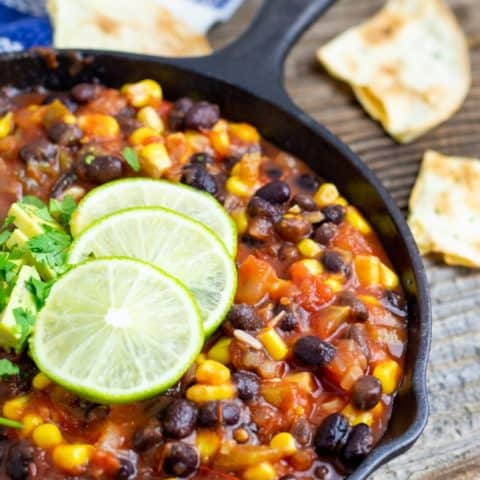 vegan salsa chili in cast iron pan with lime on wood table