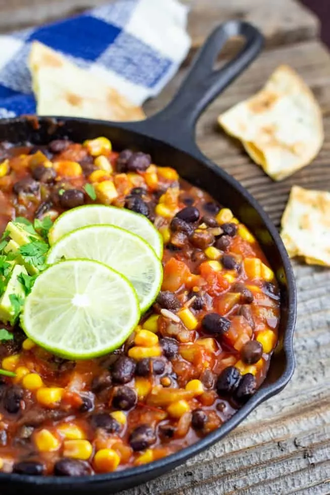 vegan salsa chili in cast iron pan with lime on wood table