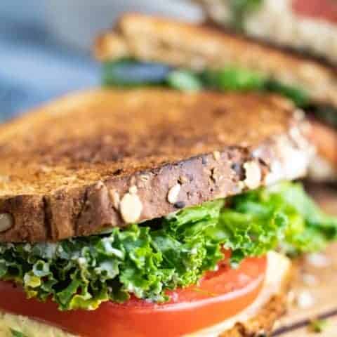 vegan grill cheese sandwich with tomato and kale on wooden board