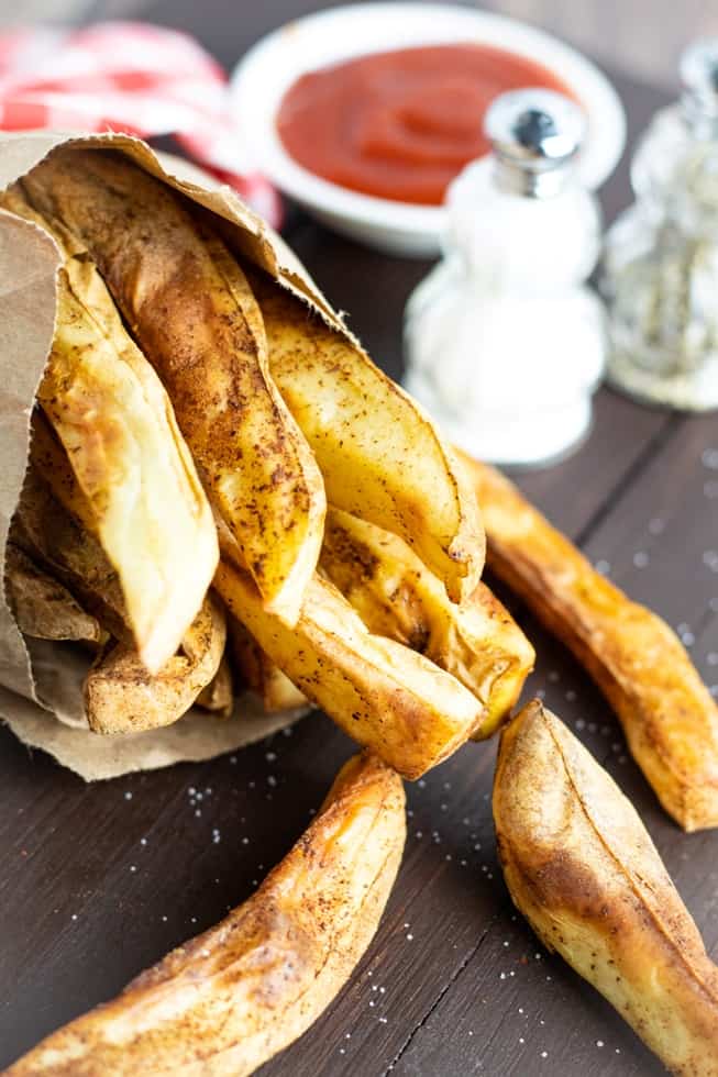 oil free french fries in brown paper bag spilled out on wooden table