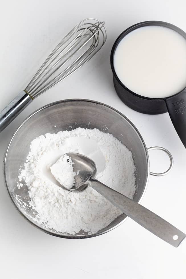 arrowroot thickener in stainless bowl beside plant milk and whisk on white background