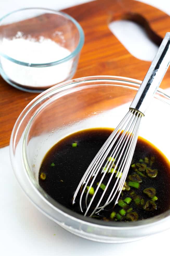 homemade stir fry sauce in bowl with whisk on white background