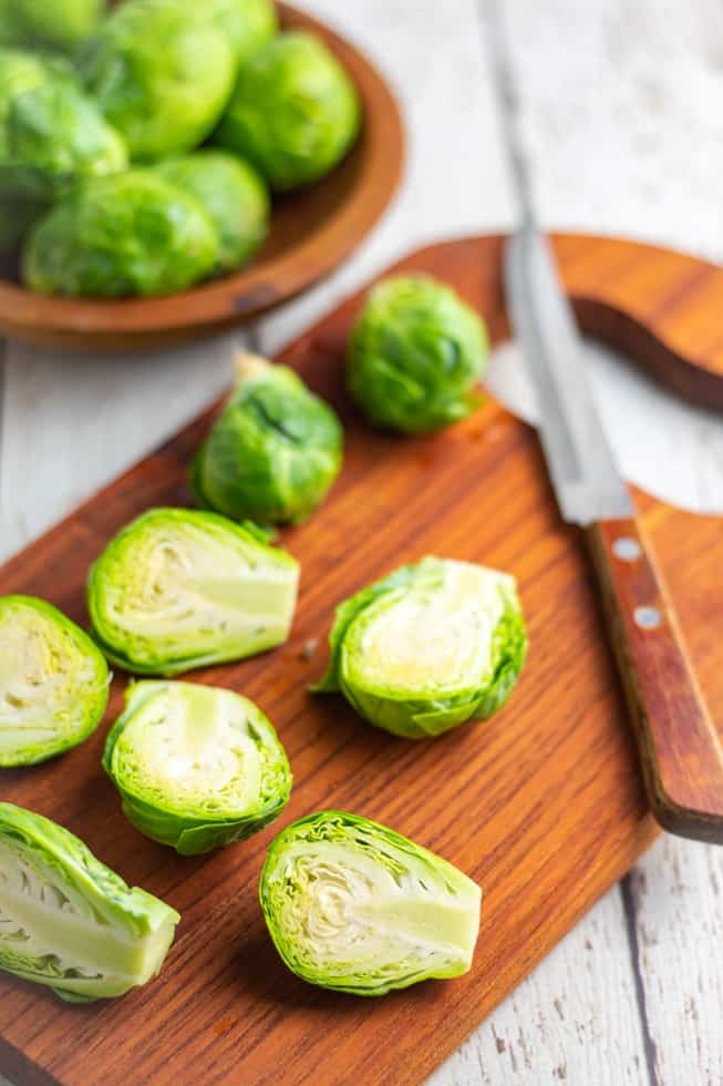 raw brussels sprouts on cutting board being sliced in half