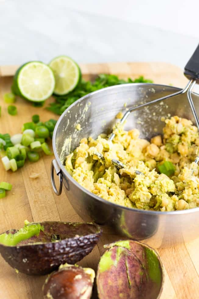 Chickpea Avocado Salad being mixed in bowl with avocado shell on table