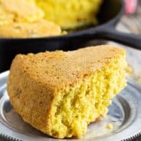 vegan cornbread slice on silver plate with cast iron pan in background