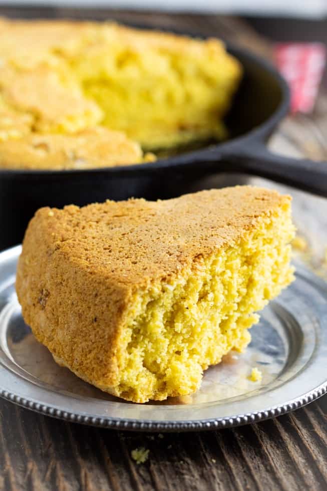 vegan cornbread slice on silver plate with cast iron pan in background
