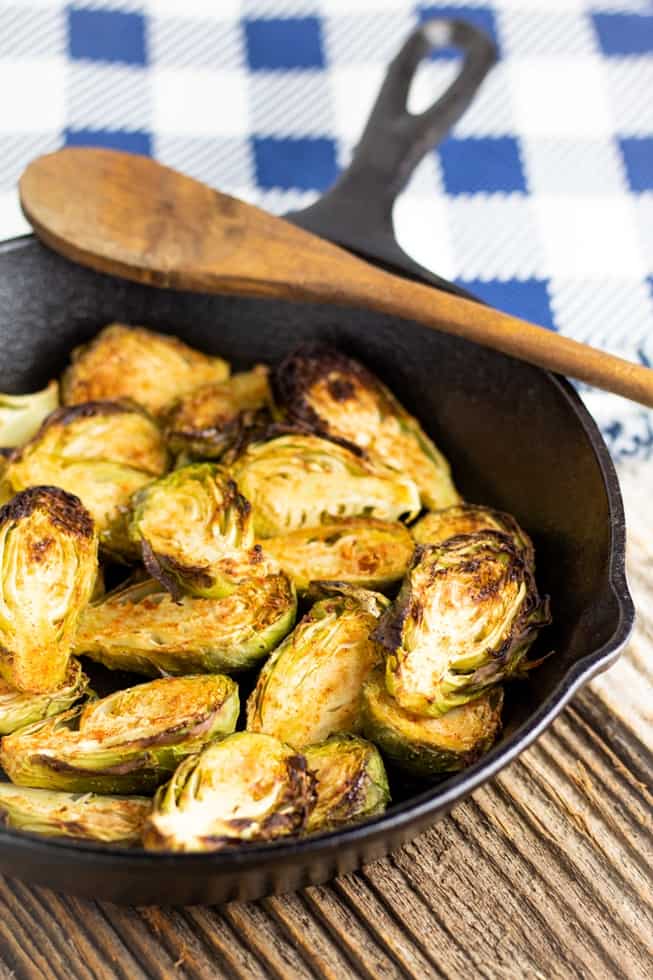sliced brussels sprouts in cast iron pan on wooden table with wooden spoon