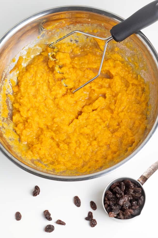 sweet potato muffin batter in stainless bowl with potato masher on white background
