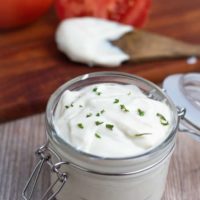 vegan mayo in glass jar with tomatoes in background on wooden table