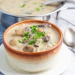 mushroom soup in bowl topped with fresh parsley with pot of soup in background