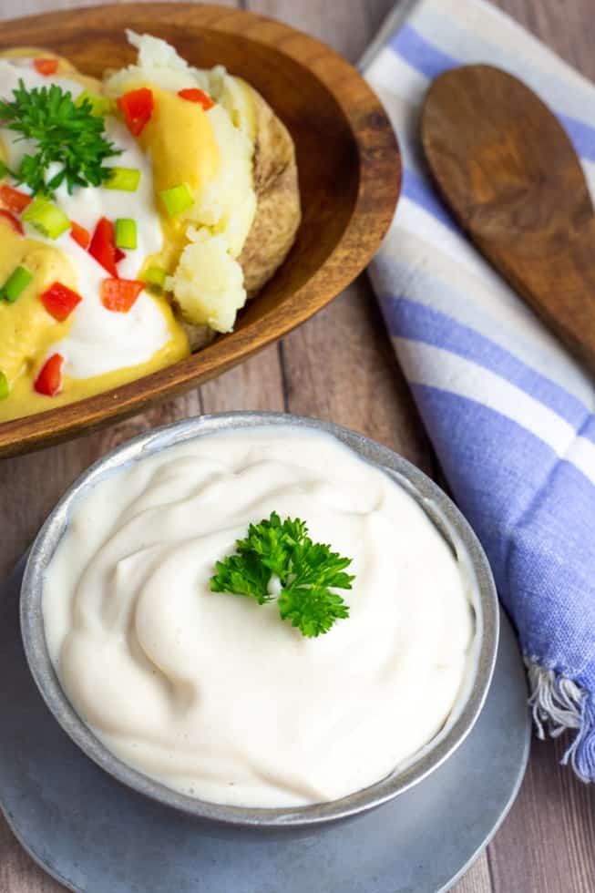 vegan sour cream in silver bowl with loaded baked potato in background