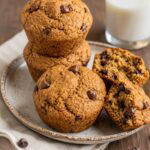 vegan chocolate chip muffins stacked on a plate with one cracked open.
