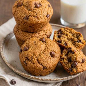 vegan chocolate chip muffins stacked on a plate with one cracked open.