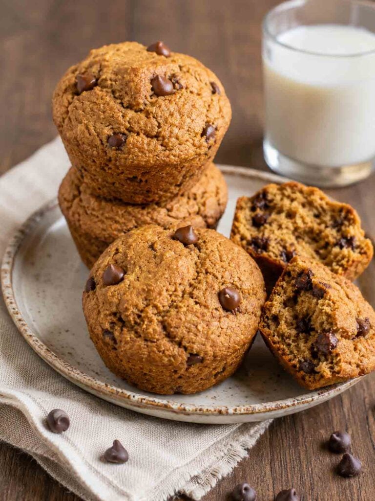 vegan chocolate chip muffins stacked on a plate with one cracked open.