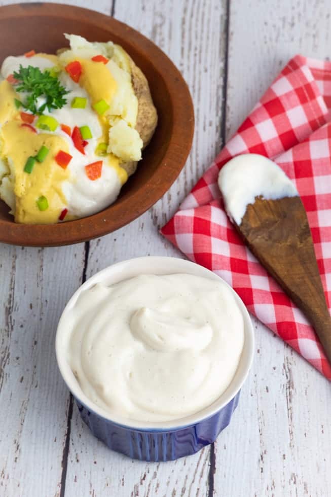vegan sour cream on white wooden table with loaded baked potato in background
