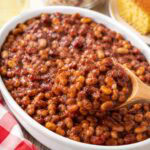 baked beans in an oval white serving dish with a wooden spoon.