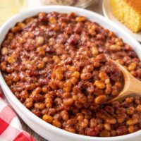 baked beans in an oval white serving dish with a wooden spoon.