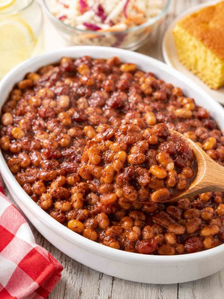 baked beans in an oval white serving dish with a wooden spoon.