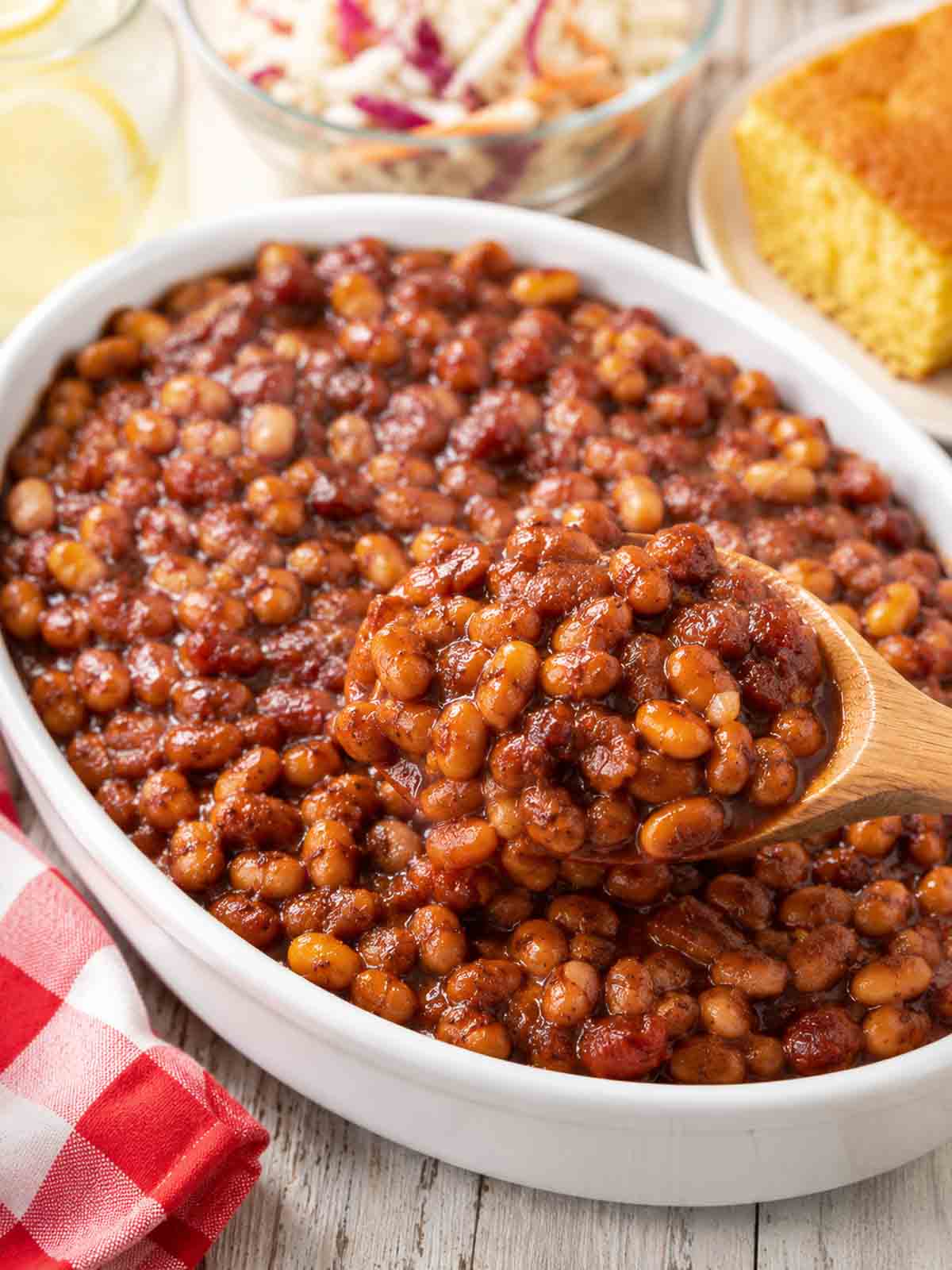 baked beans in an oval white serving dish with a wooden spoon.