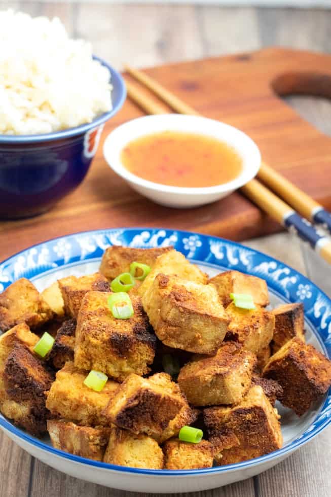 air frier tofu on blue asian bowl with chopsticks and dipping sauce in background