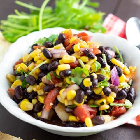 black bean corn salad in white bowl with cilantro in background