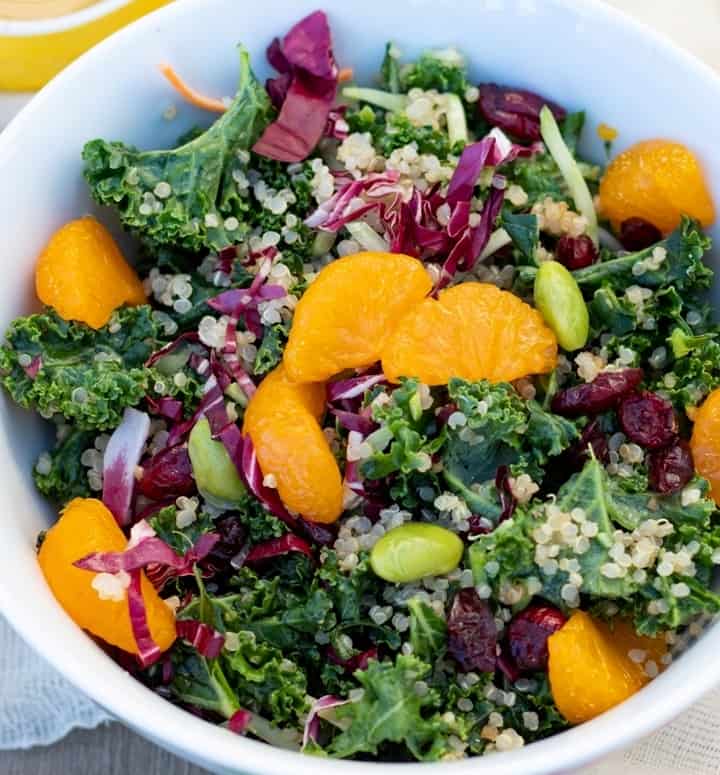 kale salad with quinoa and orange slices in white bowl