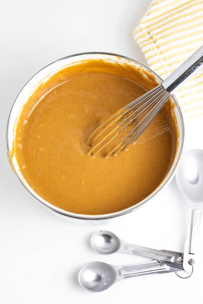 peanut sauce in bowl with whisk on white background