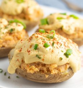 close up of vegan baked potatoes loaded with vegan cheese and spices topped with green chives
