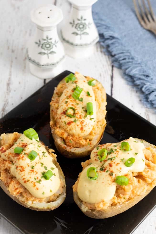 vegan baked potatoes loaded with vegan cheese on black square plate