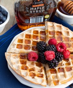 round vegean waffles topped with blackberries raspberries, and maple syrup