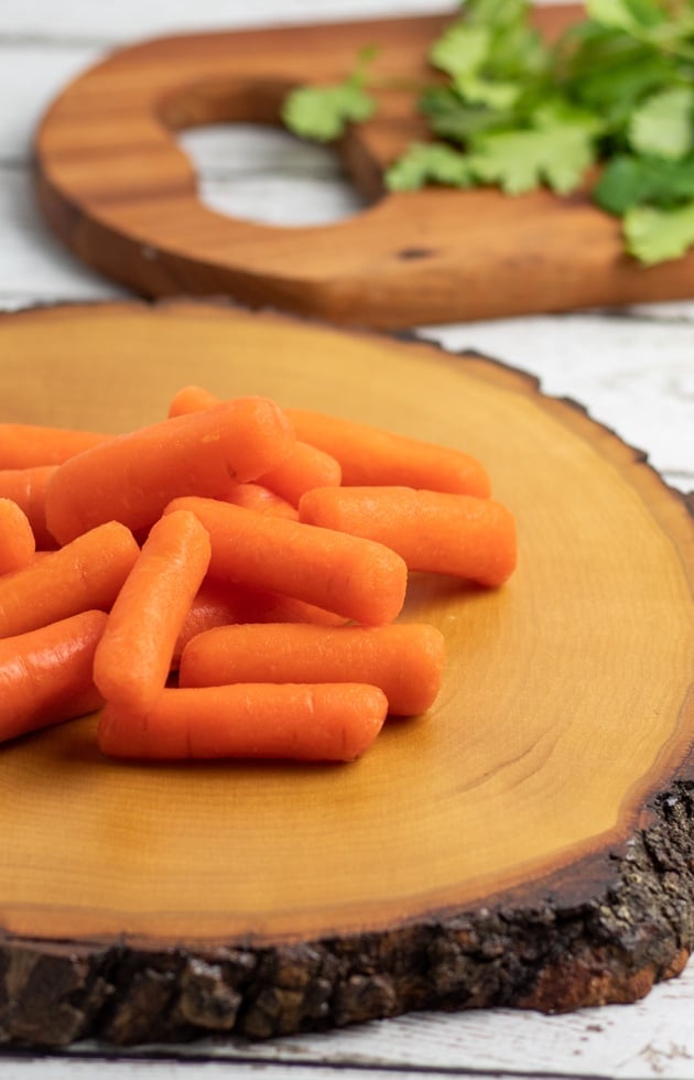 baby carrots on wooden stump with cutting board in background