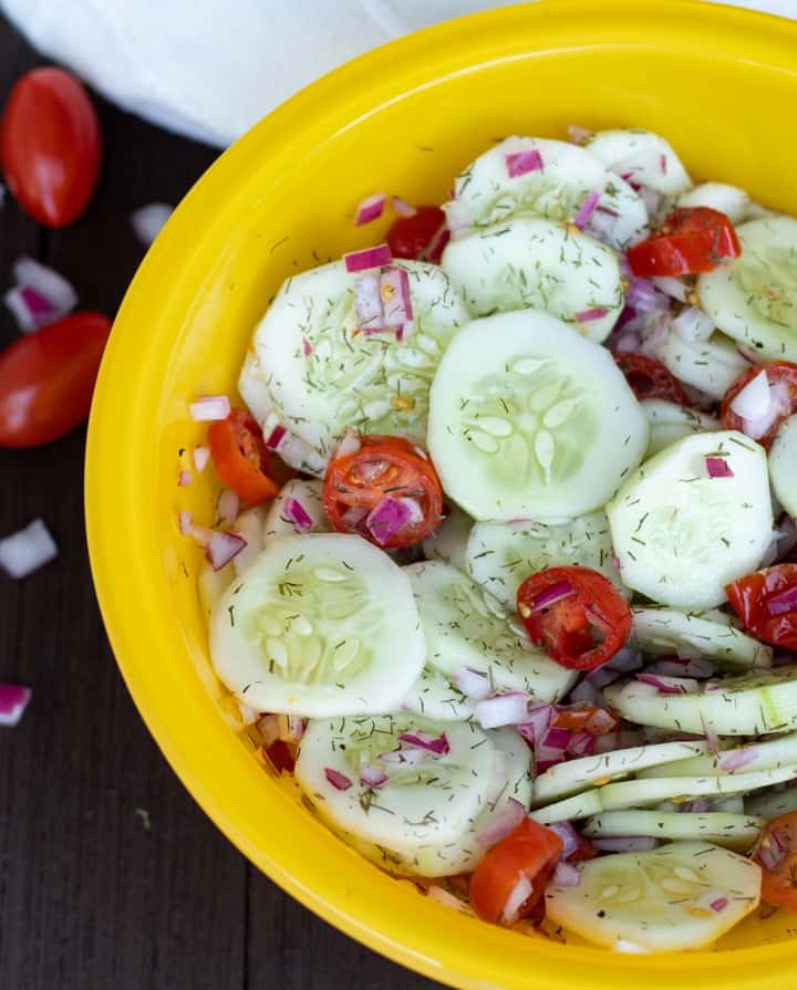 cucumber tomato salad with dill in a bright yellow bowl