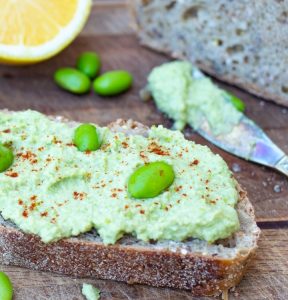 edamame hummus spread on crusty bread with spreading knive in background