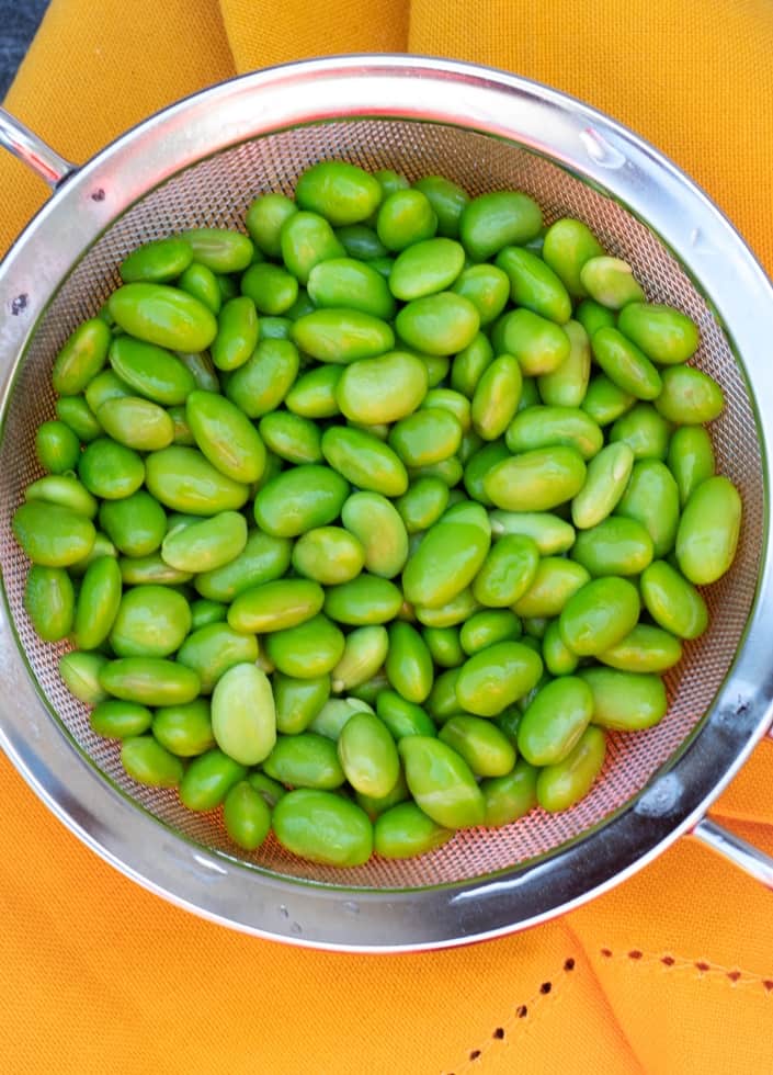 edamame beans in stainless colander on yellow napkin