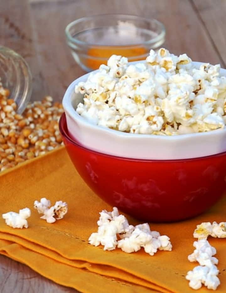 air popped corn in red bowl with popped kernels around