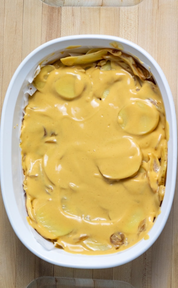 scalloped potatoes covered in vegan cheese in white casserole dish