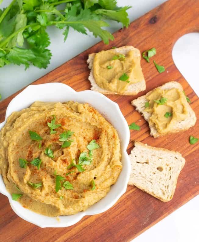 no tahini italian hummus in white bowl surrounded by melba toast topped with hummus and cilantro